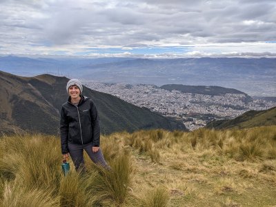 A woman stands in a mountain setting with the city of Quito visible in the background